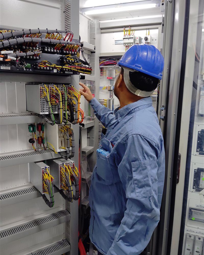 An electrician checks the wiring of a labelled control panel.