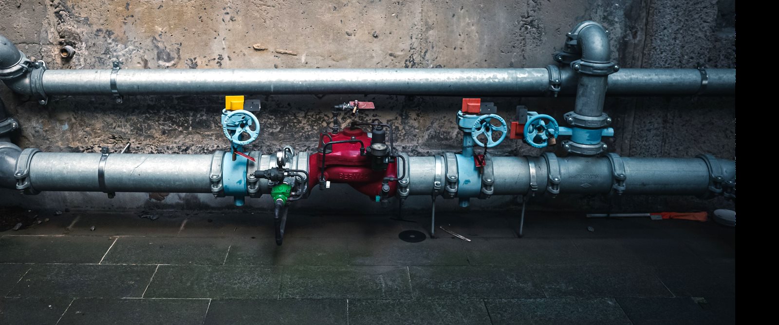 A water line with isolation valves runs along a building wall.
