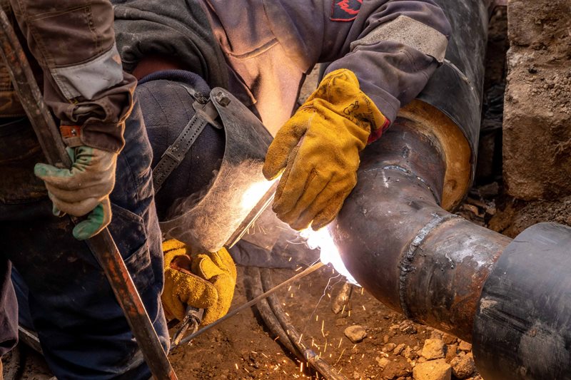A welder joins a steel pipe section on site.